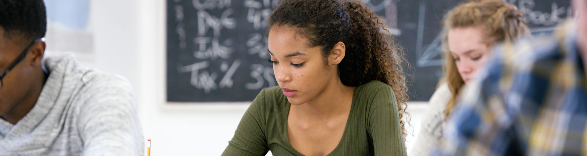 Female student wearing a green shirt sitting in a class taking notes with a pencil