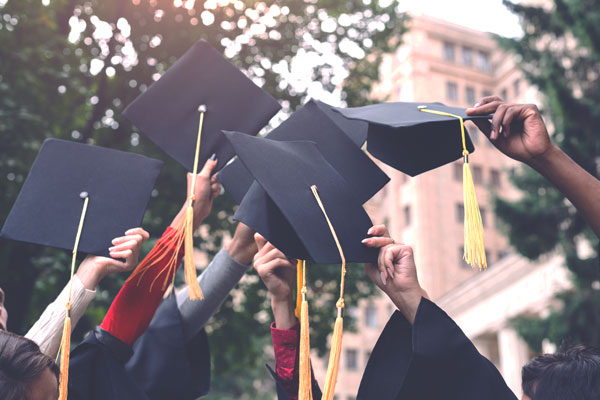 a group of student hands holding graduation caps in the air